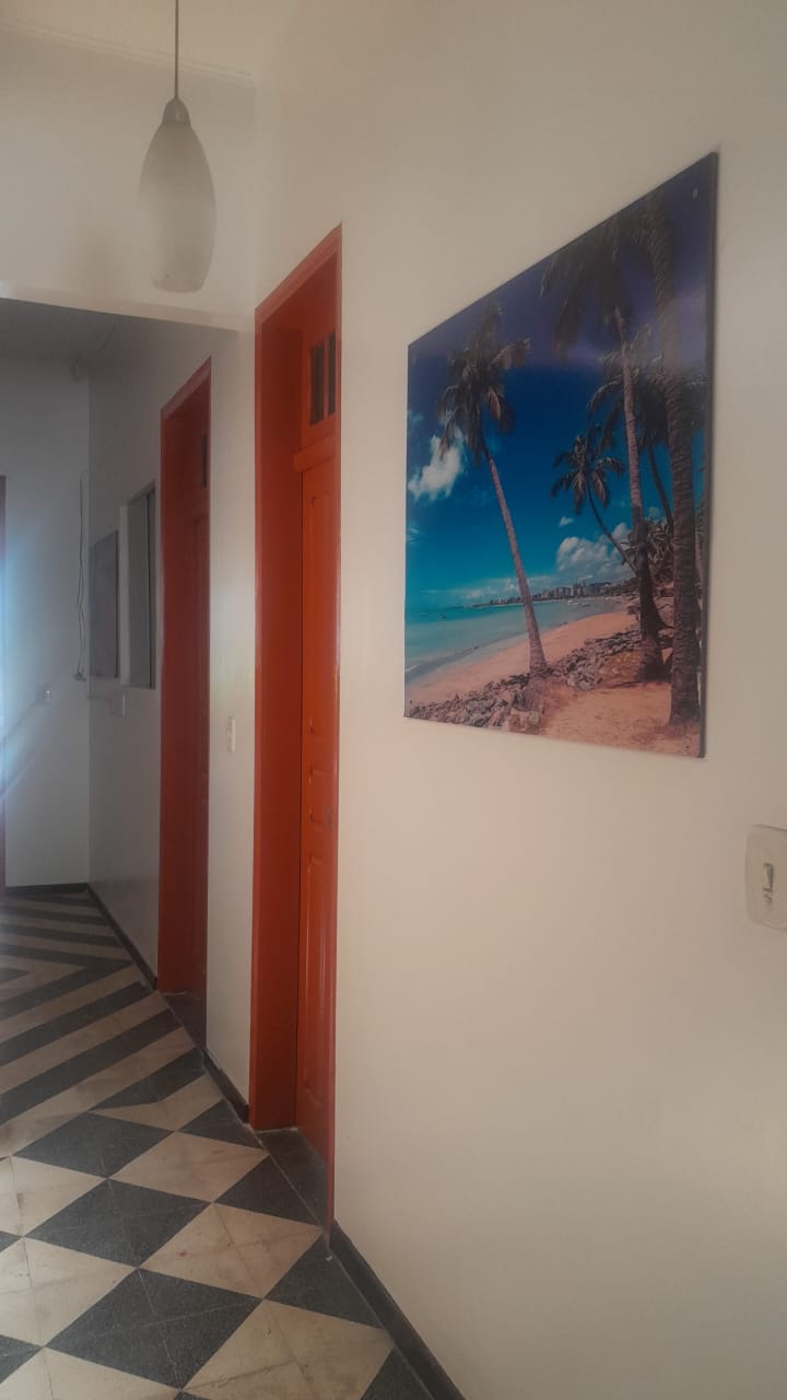 Corredor da pousada com piso xadrez e quadro da orla